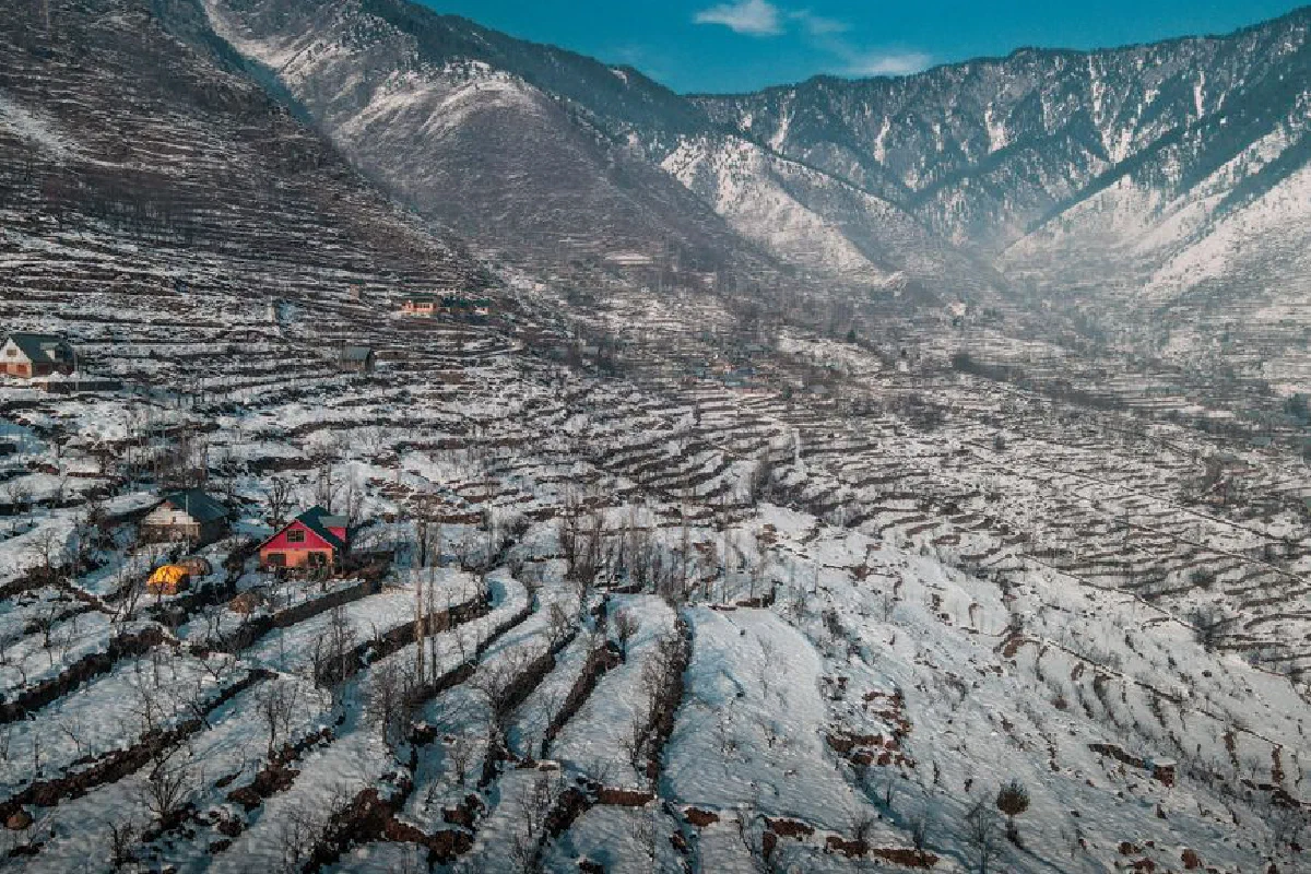 Scenery of high steep rocky slopes and wooden residential buildings in snowy mountainous terrain under blue sky