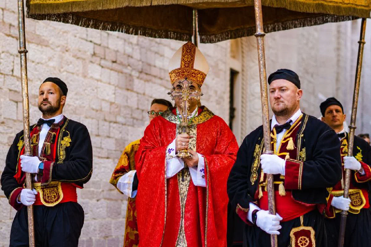 Clergy in ornate garments lead a traditional religious procession outdoors.