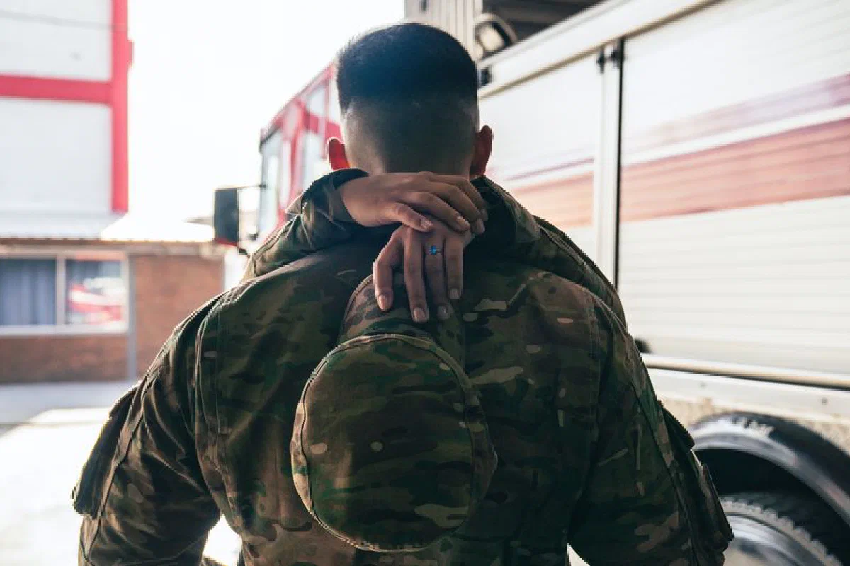 A heartfelt military reunion showing a soldier in uniform hugged from behind with a fire truck in the background.