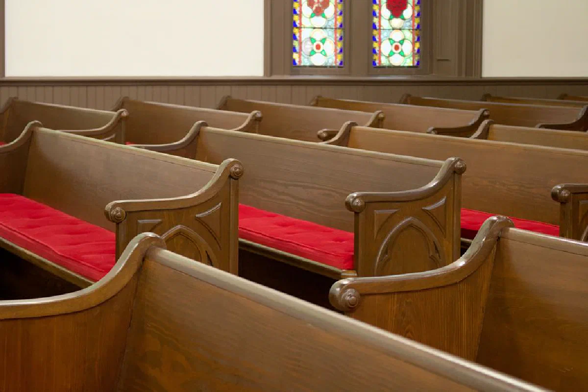 Cozy church interior with wooden pews featuring red cushions, complemented by beautiful stained glass windows.