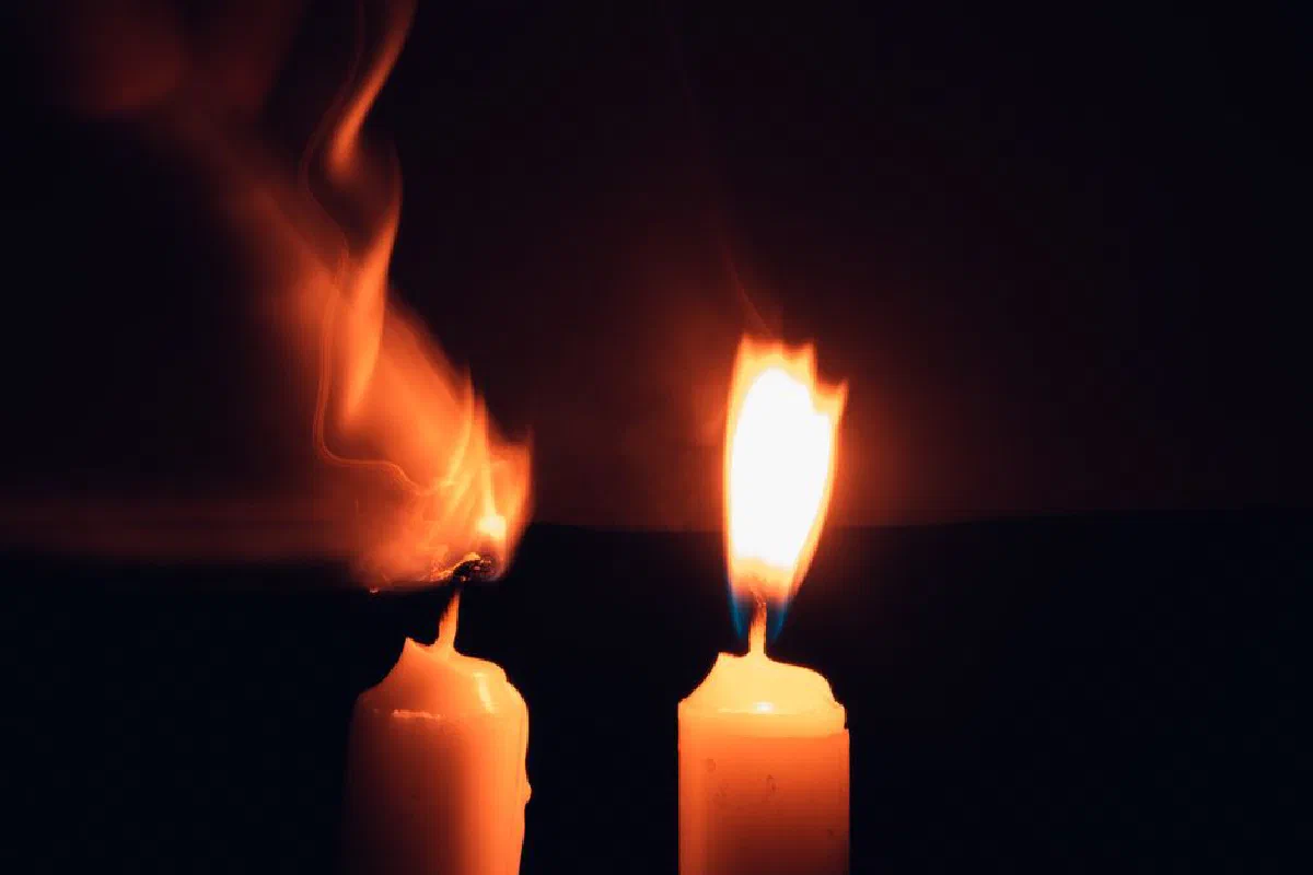 Two burning candles with flickering flames casting warm light in a dark setting.