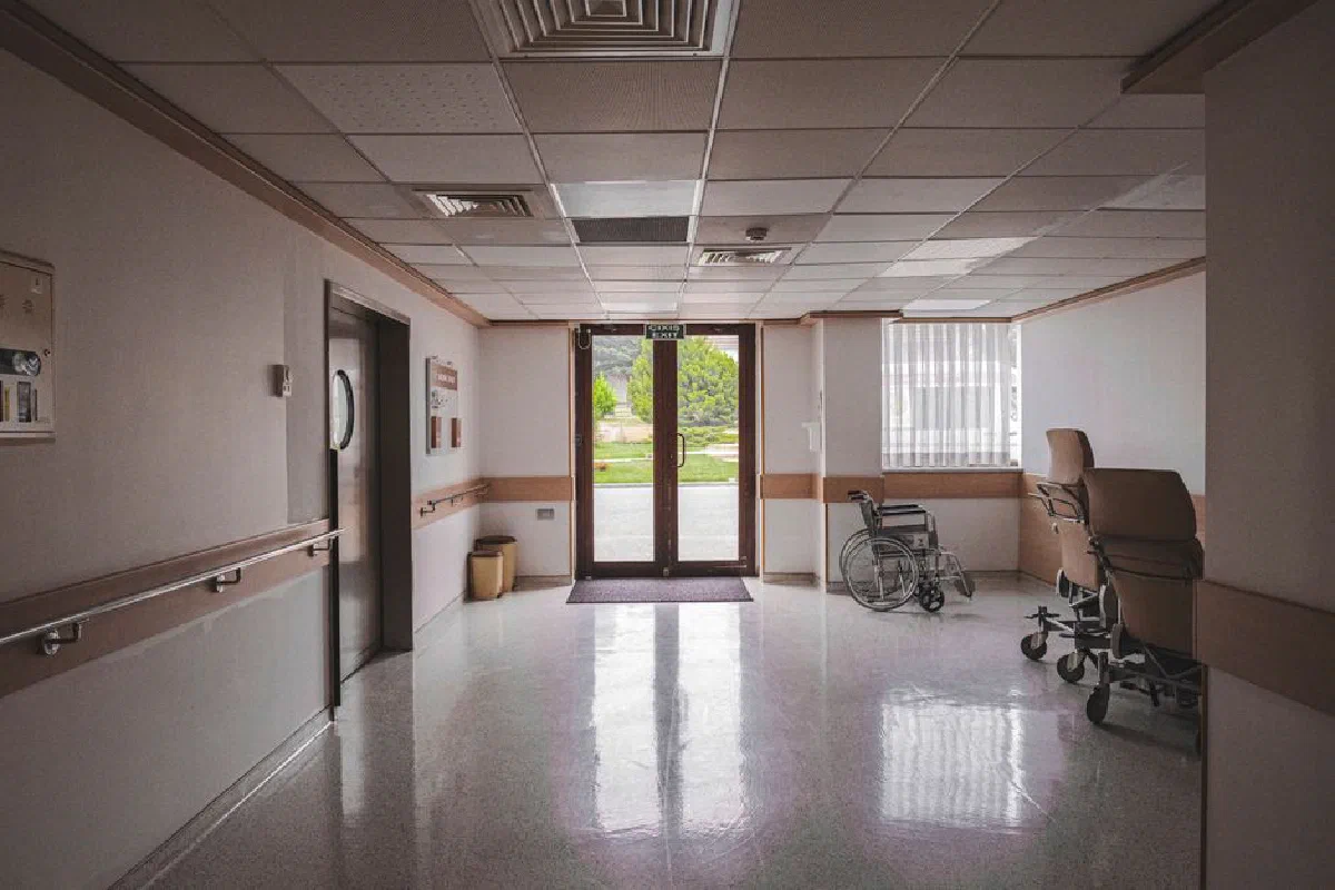 Hospital corridor with wheelchair, reflecting glass doors, and outdoor view. Ideal for healthcare themes.