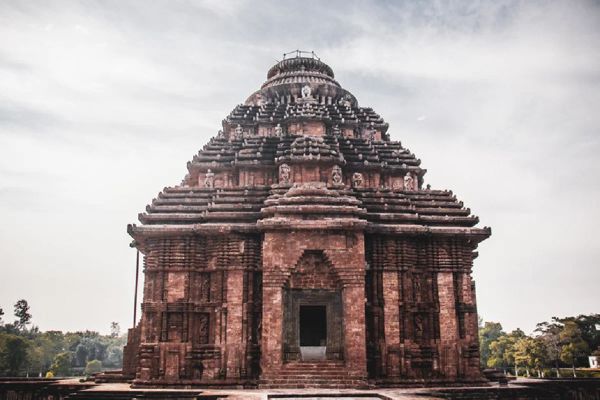 Exterior of main building of historical Hindu Konark Sun Temple with carved details and sculptures on roof against cloudy sky