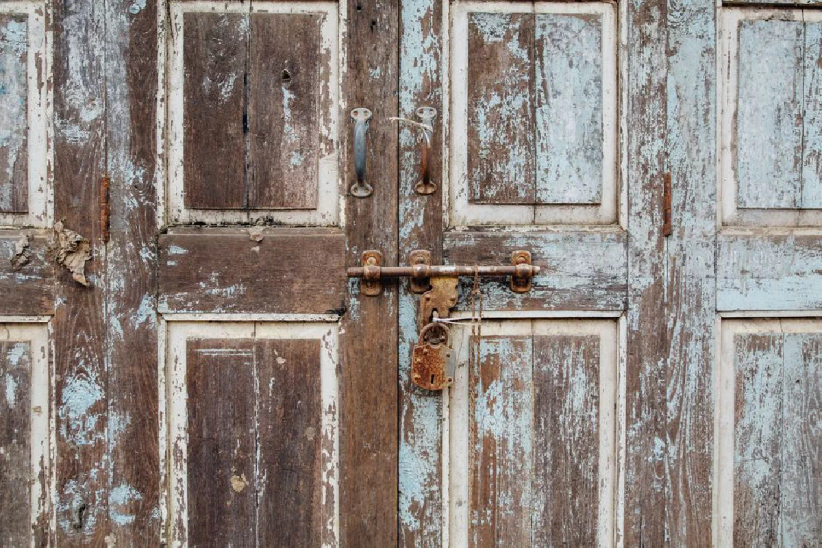 Close-up of an old wooden door with a rusty padlock, showcasing decay and texture.