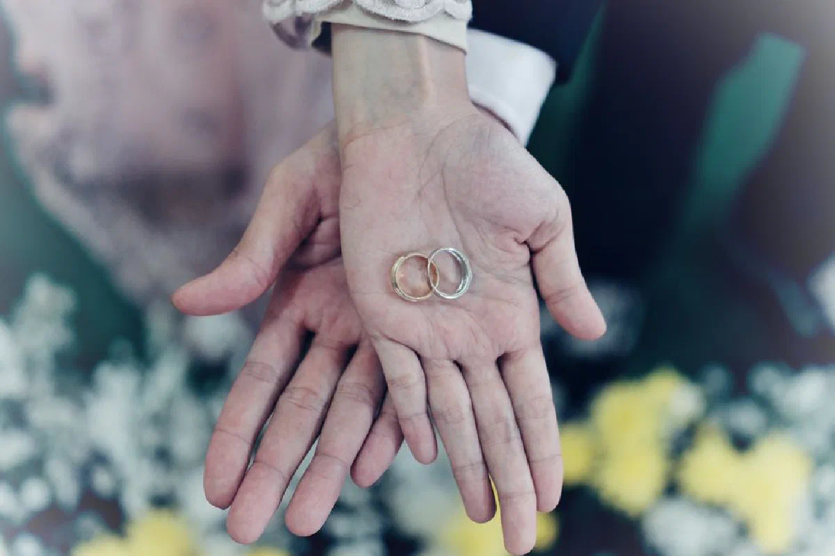 Romantic close-up of intertwined hands holding wedding rings, symbolizing love and commitment.