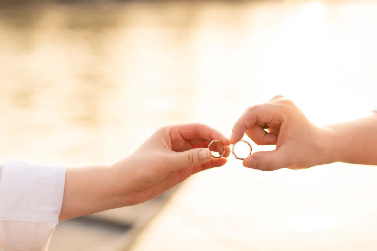 A close-up of two hands exchanging wedding rings against a sunset background, symbolizing unity.