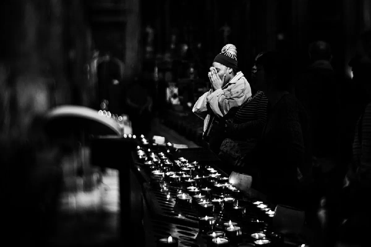 A person praying in a dimly lit church with rows of candles, captured in monochrome.