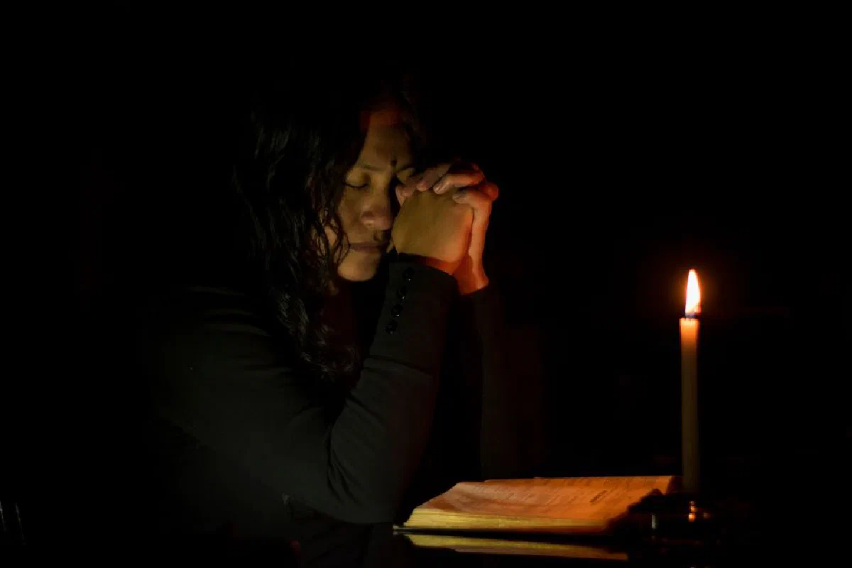 A woman deeply immersed in prayer by candlelight, evoking a serene and contemplative mood.