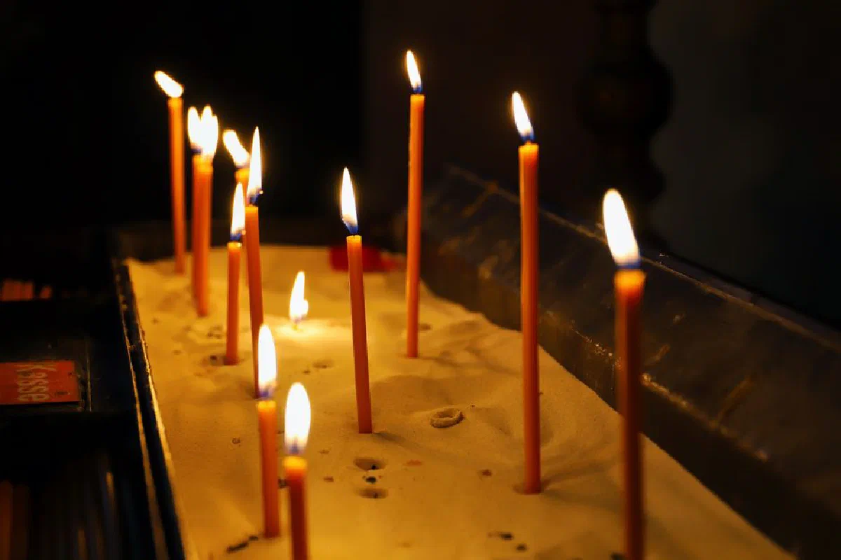Illuminated votive candles in sand create a serene spiritual ambiance in a dimly lit setting.