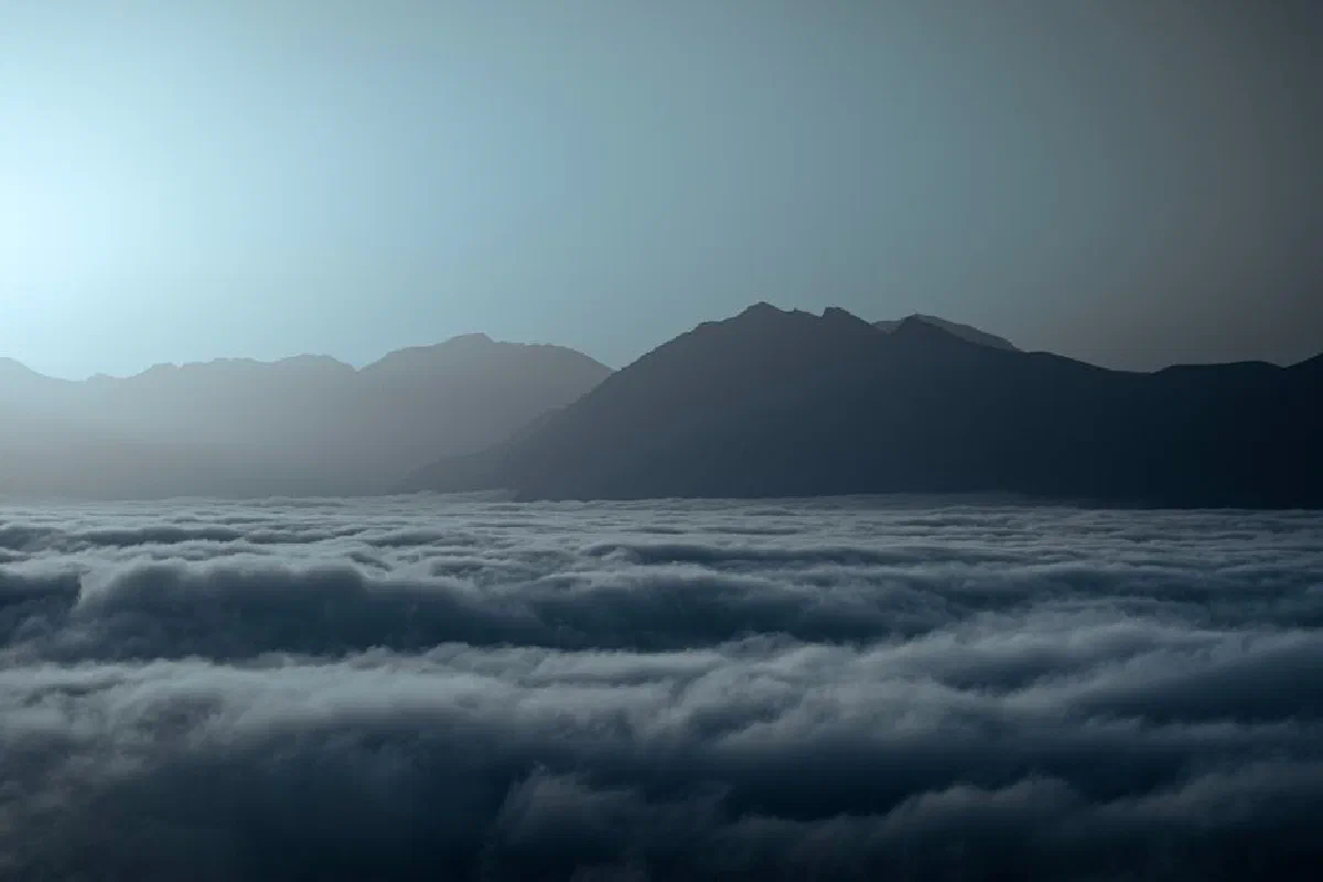 Serene landscape of mountains peeking through misty clouds at twilight creating a tranquil scene.