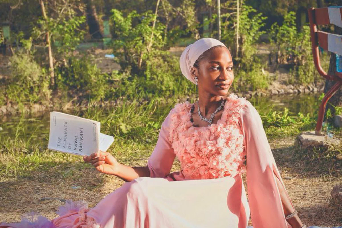 Sophisticated woman in a pink dress reading a book outdoors on a sunny day.