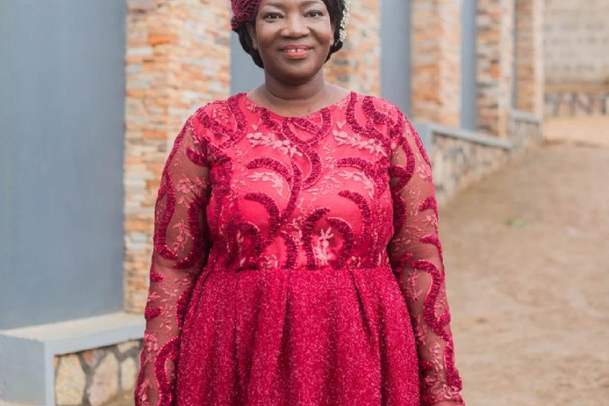 An elegantly dressed African woman in a vibrant red gown stands outdoors, exuding confidence and grace.