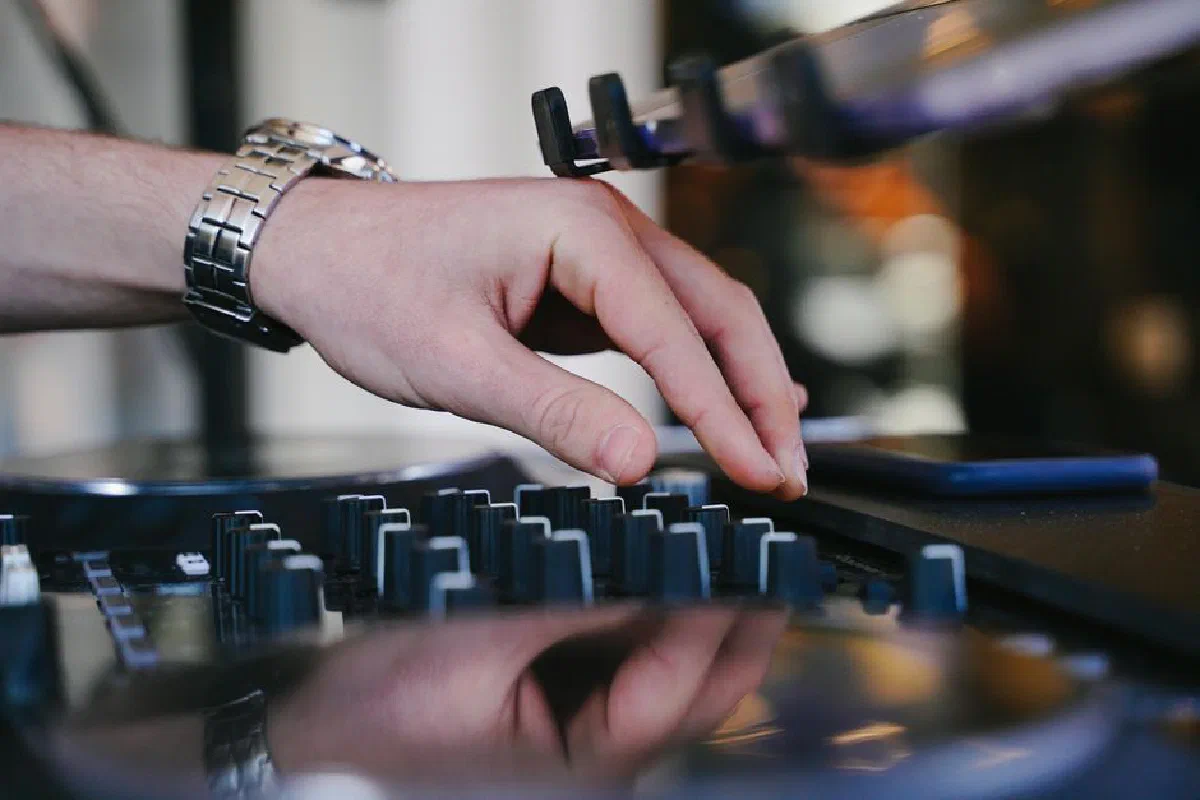 Close-up of a DJ's hand adjusting knobs on a mixer for live electronic music performance.