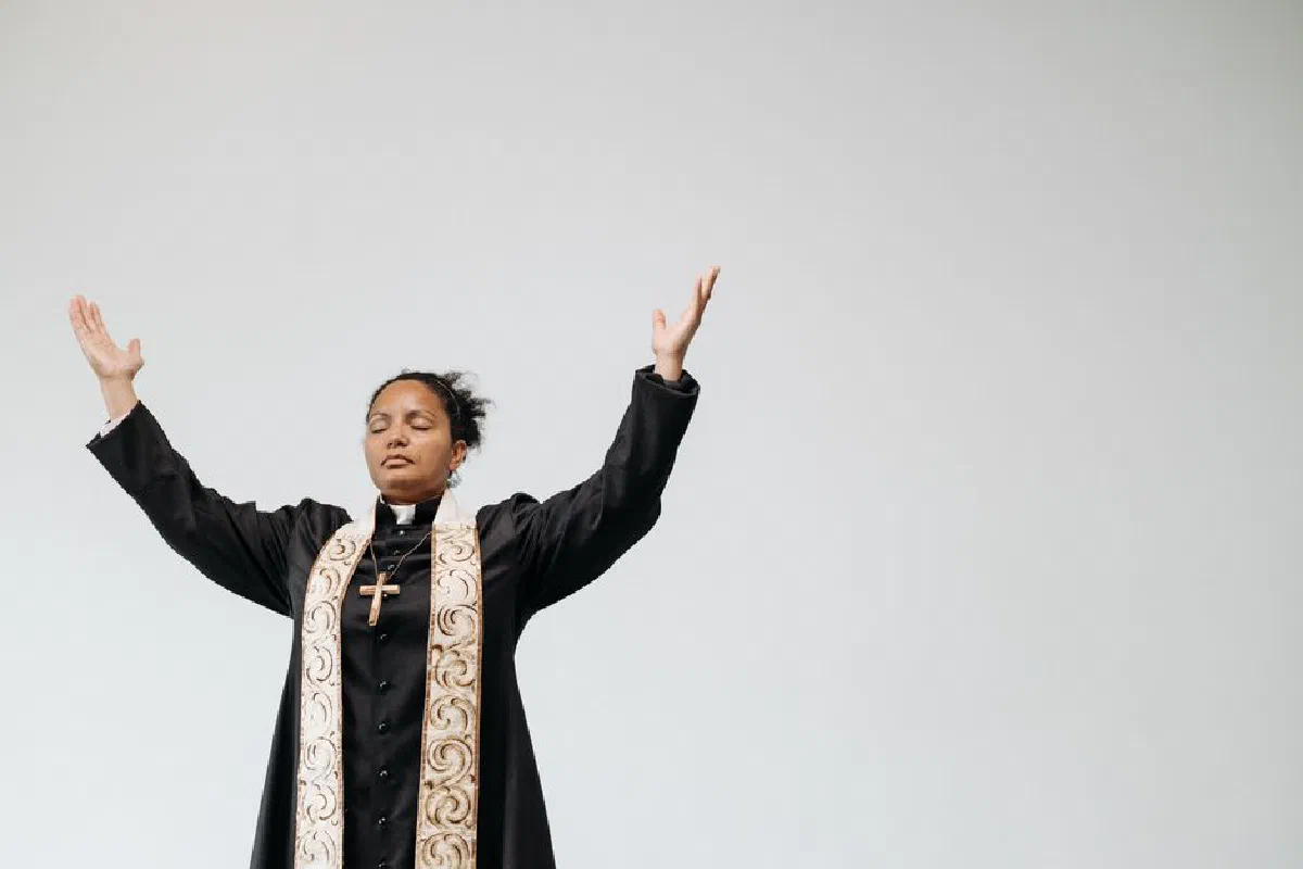 Female pastor in cassock praying with raised hands, symbolizing faith and devotion.