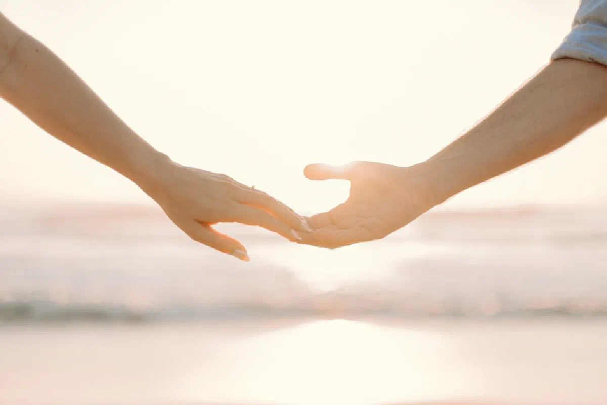Romantic moment of hands reaching towards each other against a sunset beach backdrop.