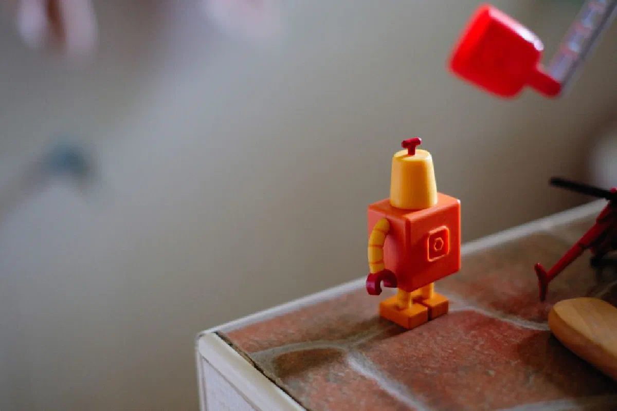Close-up of a small colorful robot toy standing on a brown surface indoors.