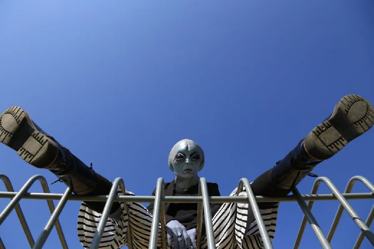 Low angle shot of a person in an alien costume sitting on a metal structure against a clear blue sky.