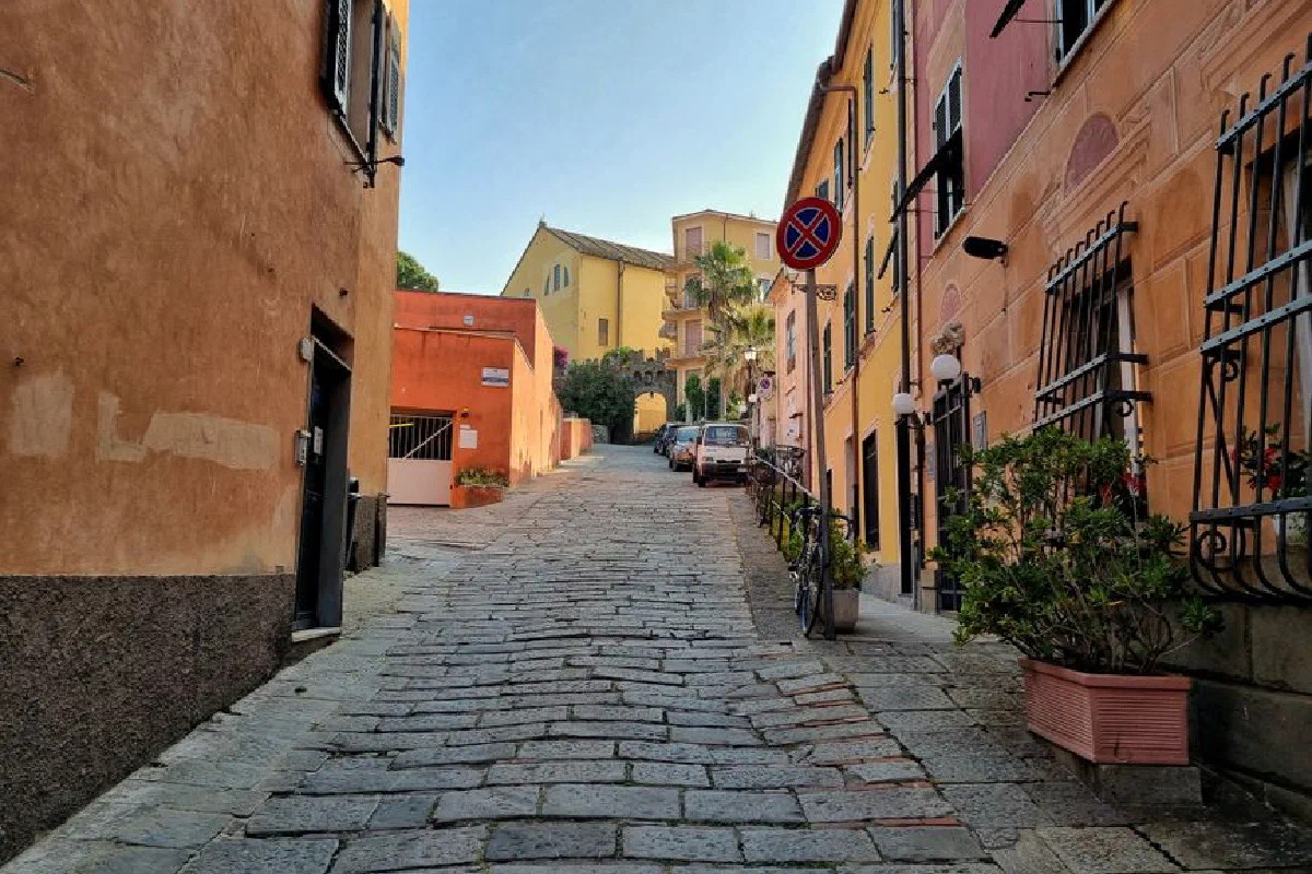 Cobblestone street in Liguria with colorful buildings and bright sunlight.