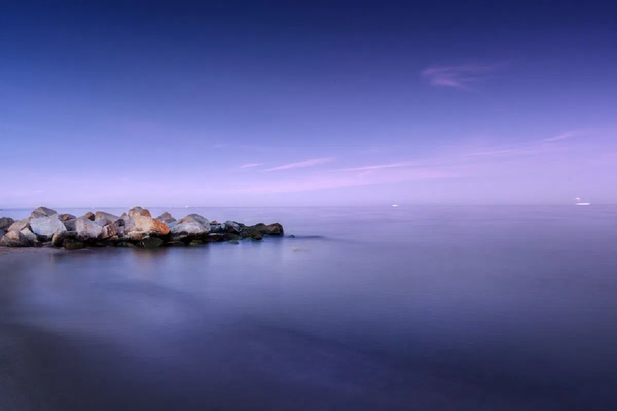 Breathtaking seascape with rocks placed on coast near calm water under blue sky in daytime