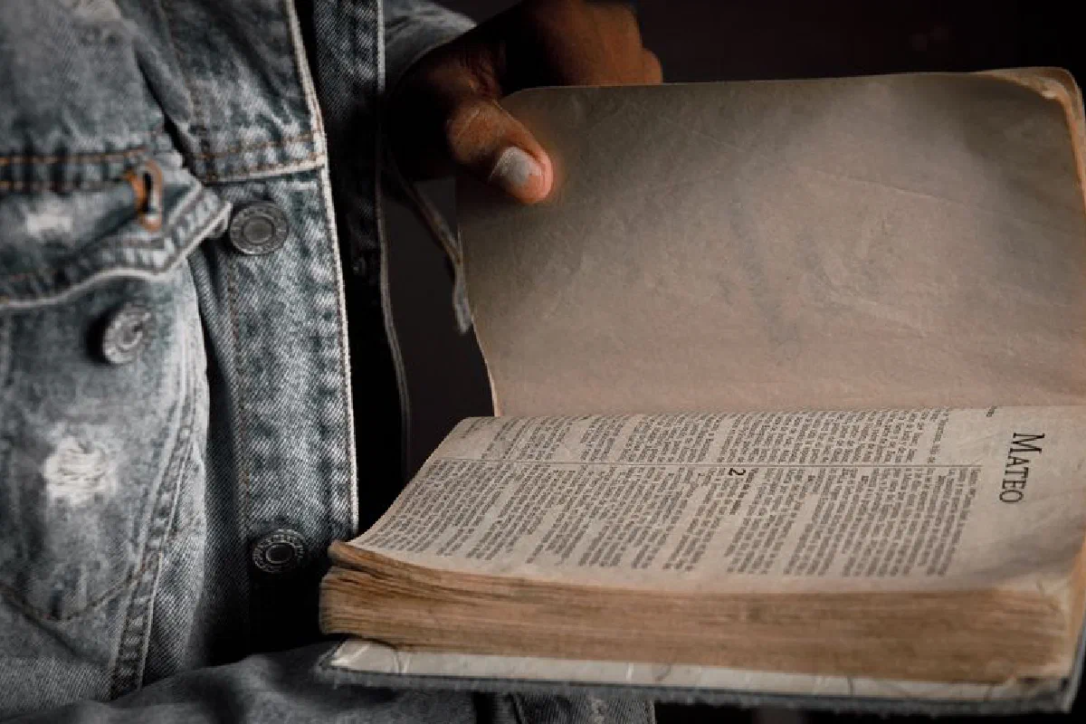 A person in a denim jacket holding an open Bible to the book of Matthew.