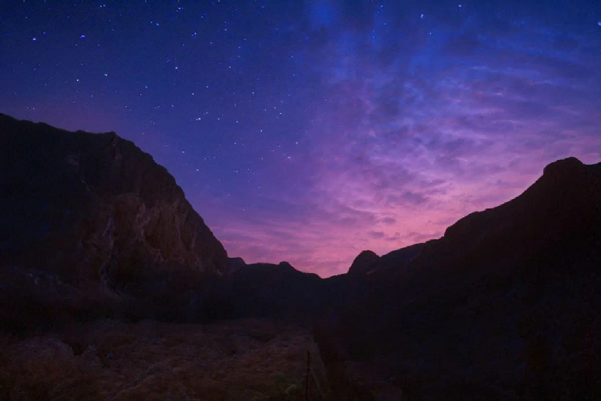 A dramatic silhouette of mountains against a starry purple and pink sky at dusk.