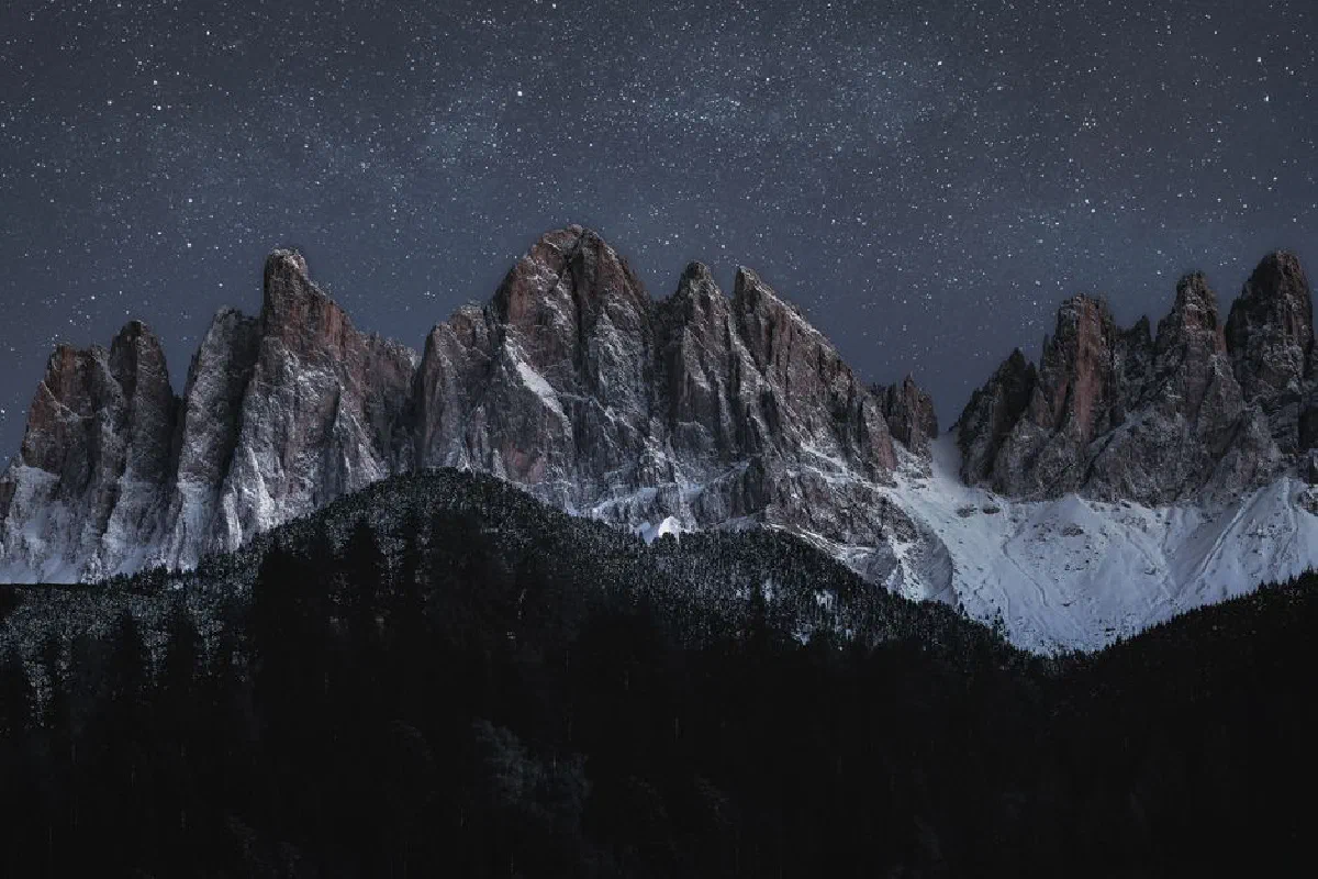 Dramatic snowy mountain peaks under a star-filled night sky, capturing nature's beauty.