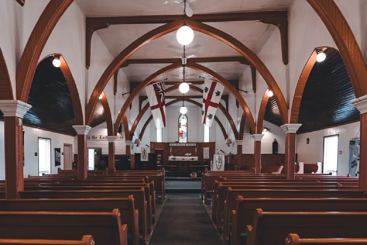 Beautiful interior view of a historic wooden church with arches, pews, and stained glass window.