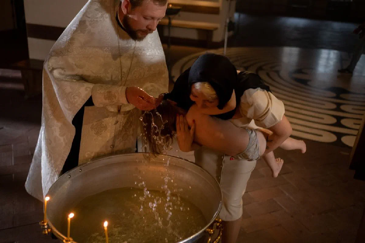 A child being baptized by a priest with family in a traditional church setting.