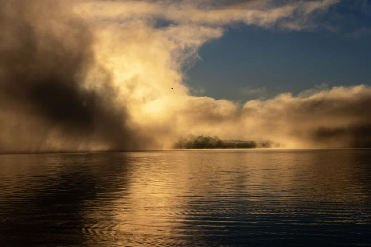 A serene lake enveloped in dramatic morning fog with golden sunlight.