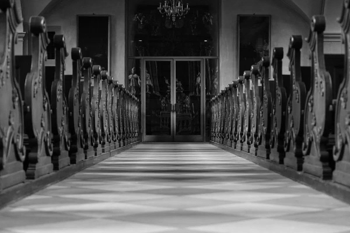 Black and white photo capturing elegant church aisle with detailed wooden pews.
