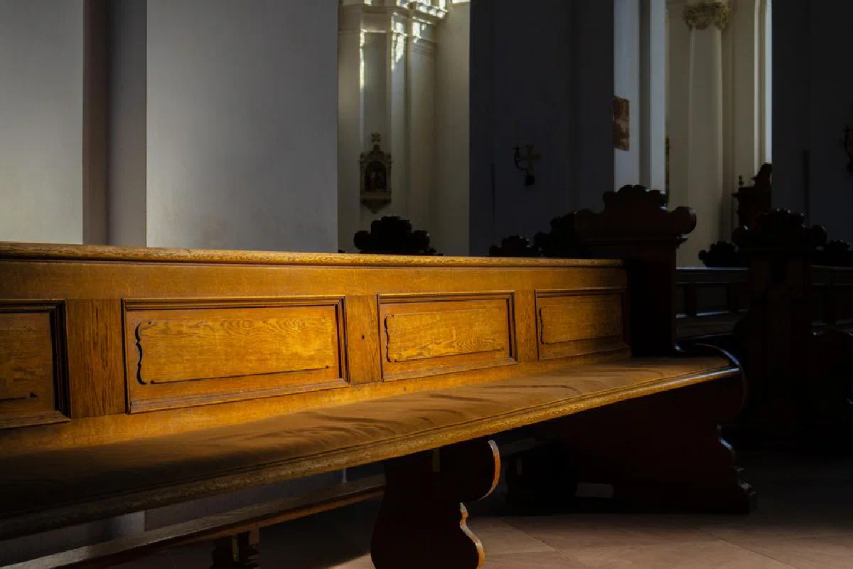 Sunlight highlighting a wooden church pew inside a historic church, creating a serene atmosphere.
