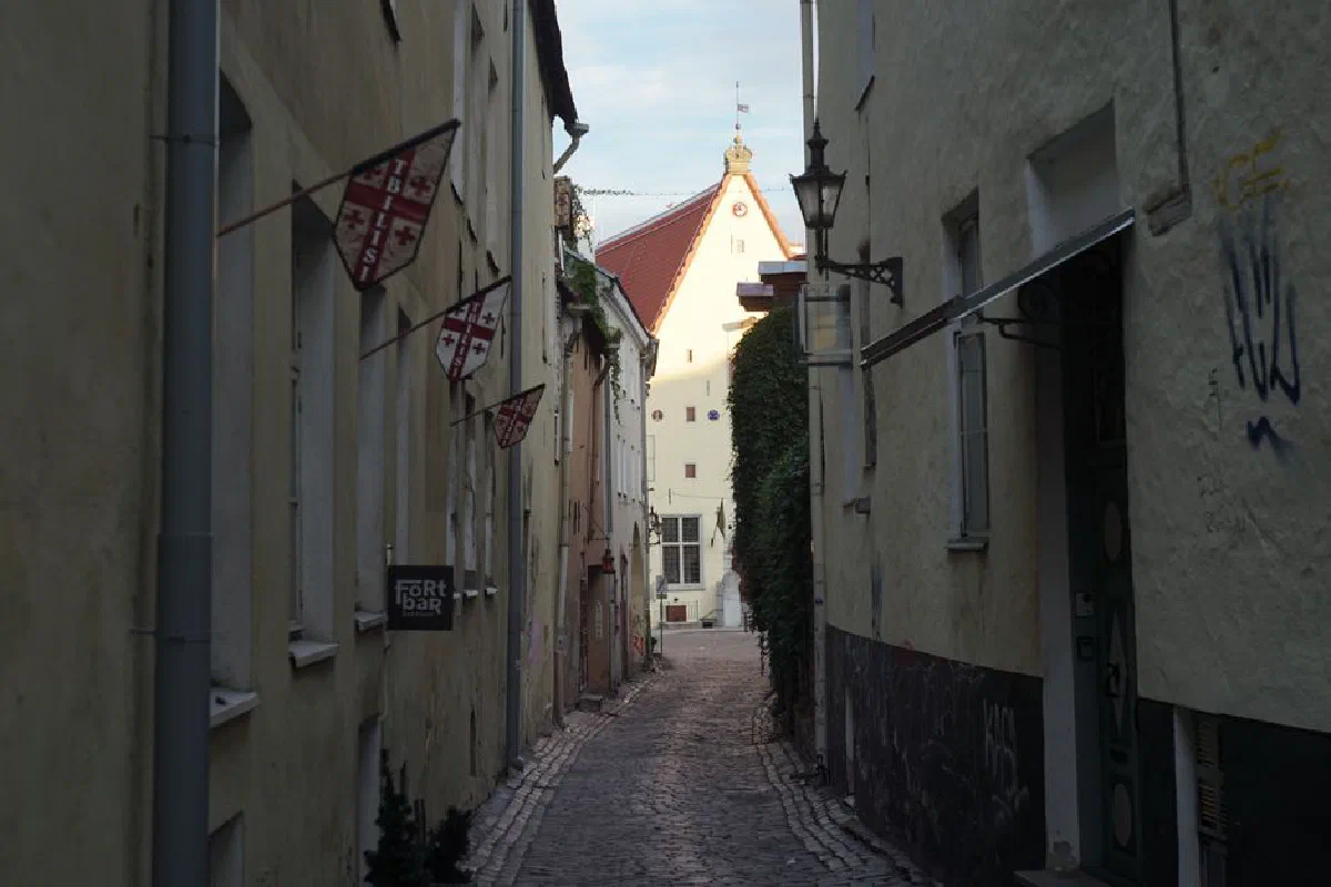 Picturesque narrow alleyway with medieval architecture and flags in a European city at sunset.