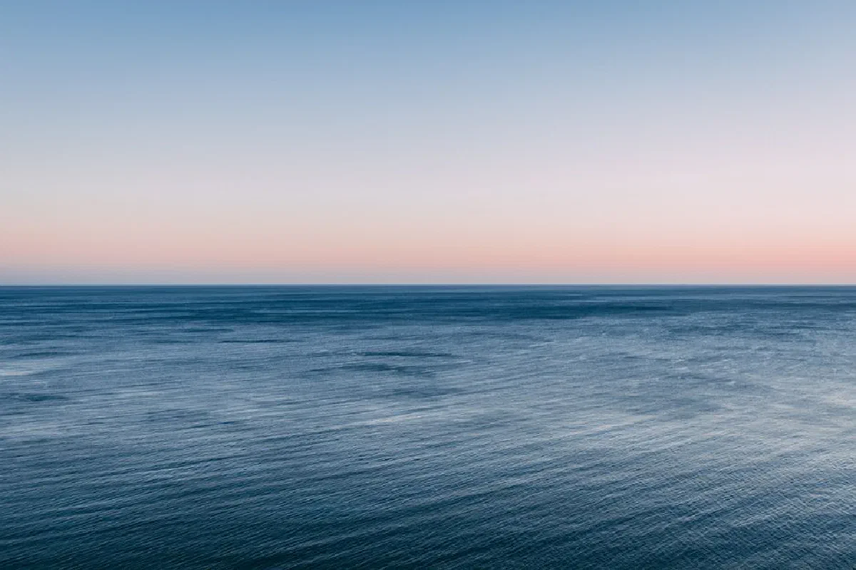 Peaceful view of the ocean at twilight with a colorful sky and calm waves.