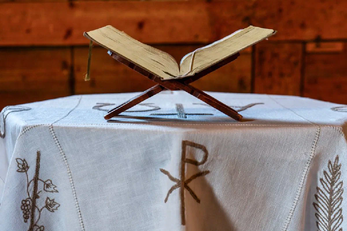 Antique Bible displayed on a wooden stand over a decorated cloth in a rustic church setting.