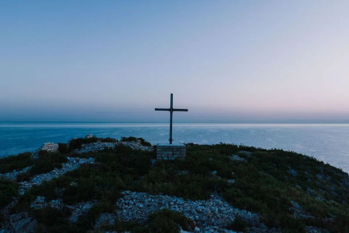 A tranquil scene of a cross on a hilltop overlooking the sea, captured at dawn in Polignano a Mare, Italy.