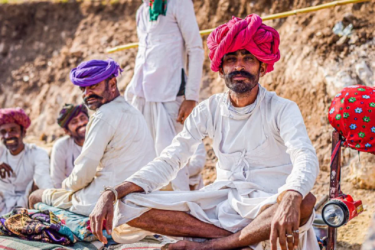 A group of Rebari men in bright turbans and traditional attire, sitting outdoors.