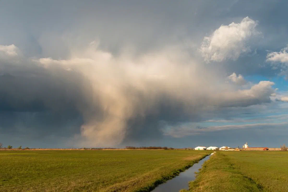 A dramatic cloud formation over a rural farm field with vivid green grass and a distant village.
