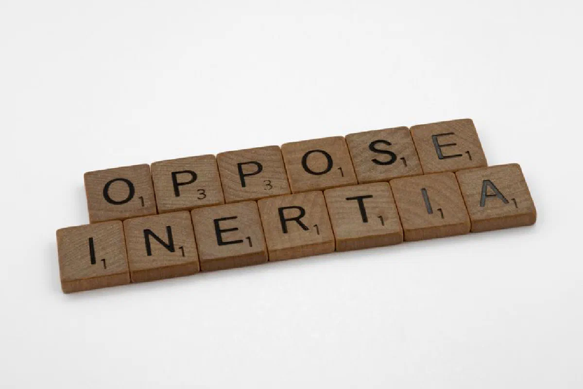 Scrabble tiles spell 'oppose inertia' on a white surface, creating inspiration.