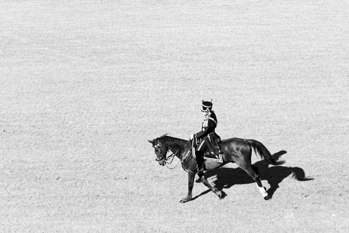 A classic black and white aerial view of a horse with a rider in uniform on an open field.
