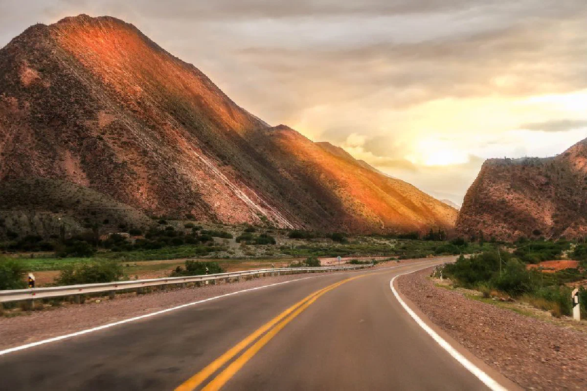 A winding road through mountains under a dramatic sunset sky, perfect for travel inspiration.