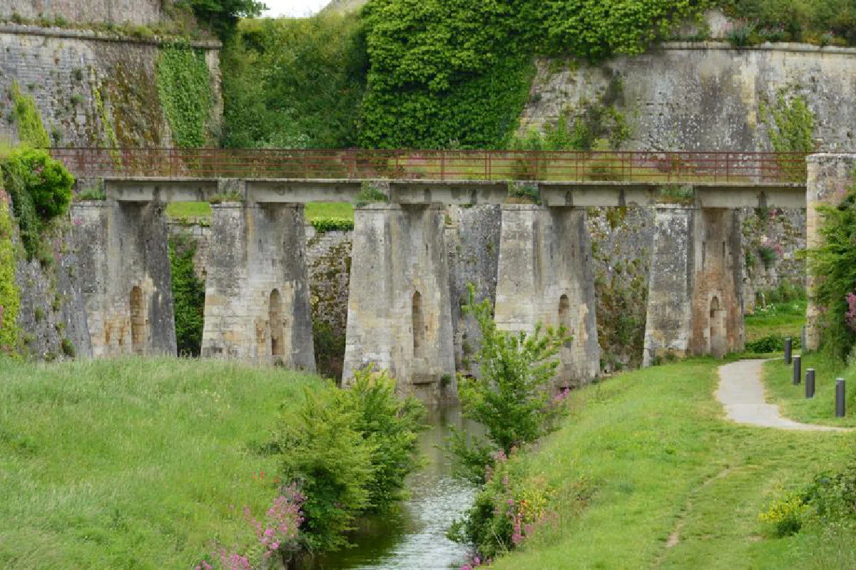 An ancient stone bridge over a small river with vibrant green surroundings and historic architecture.