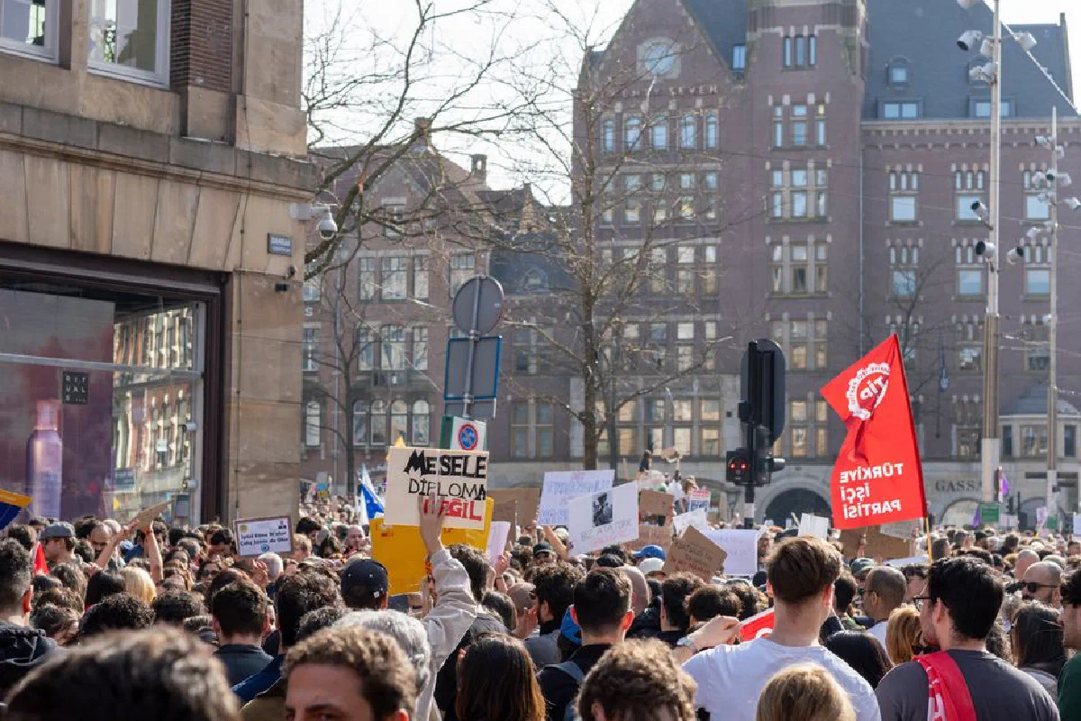 A vibrant city protest with diverse crowd holding various signs and banners under a bright day.