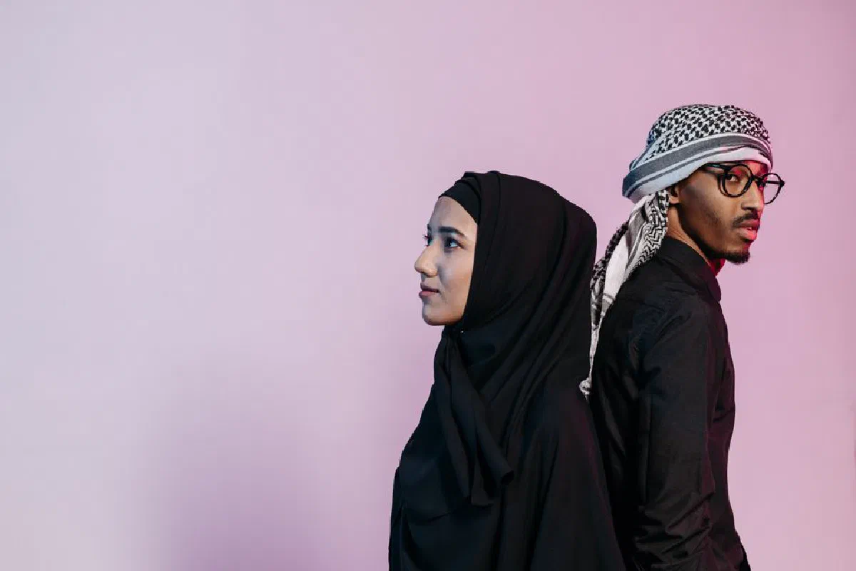 Portrait of a Muslim couple in traditional attire against a pink backdrop, showcasing cultural fashion.