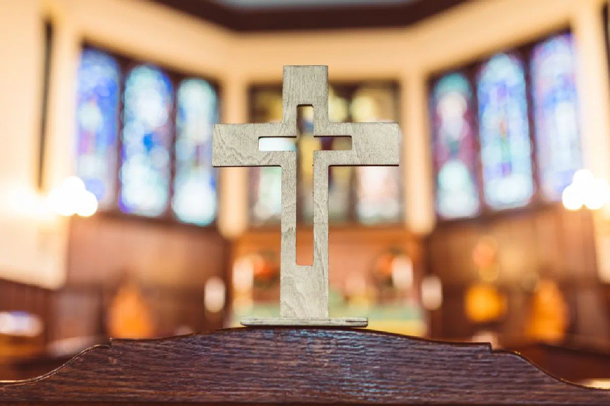 Close-up of a wooden cross inside a church with stained glass background.