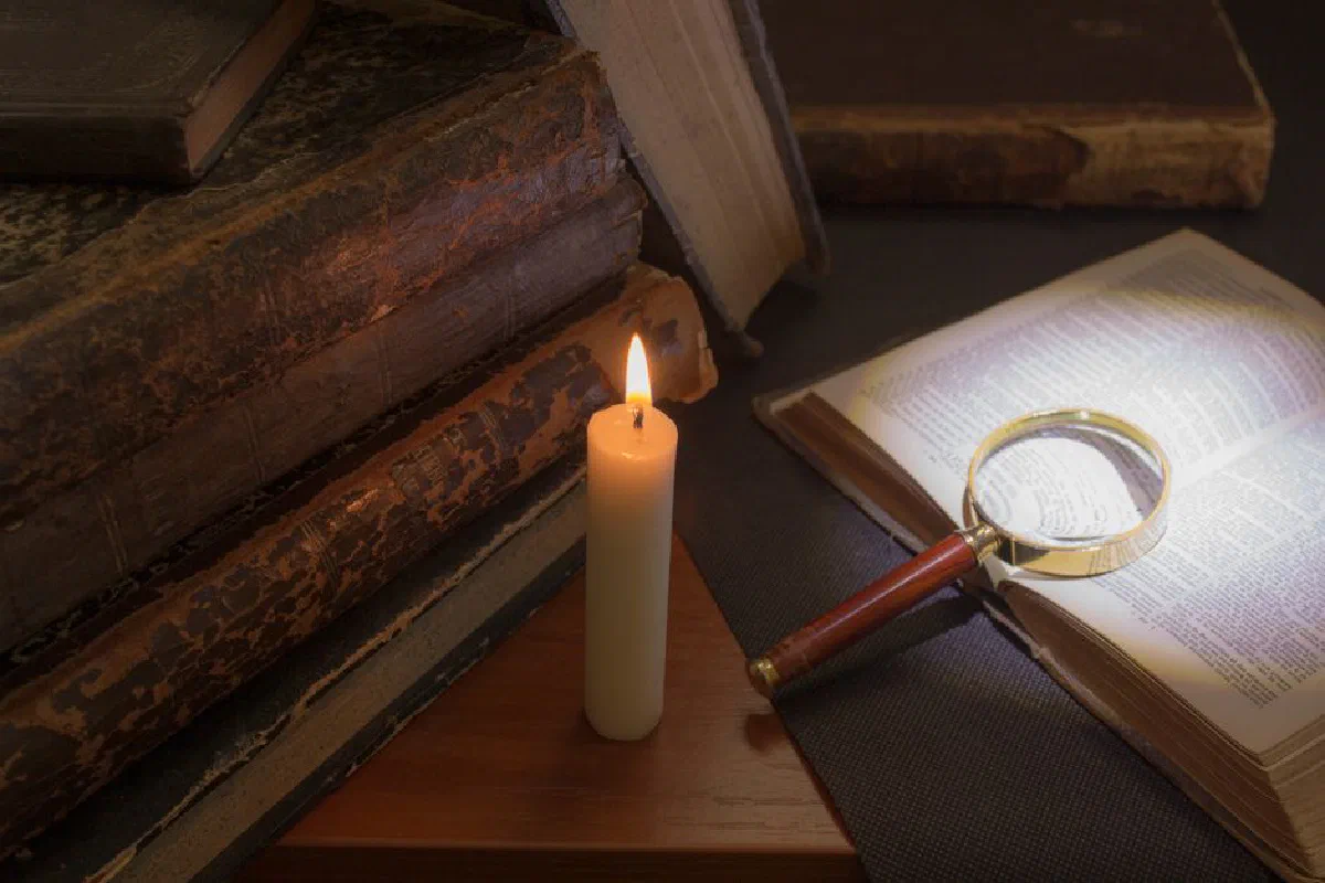 A moody scene with vintage books, a candle, and magnifying glass highlighting text.