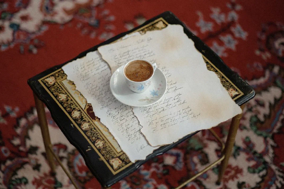 A delicate coffee cup placed on a vintage manuscript over an ornate wooden table.