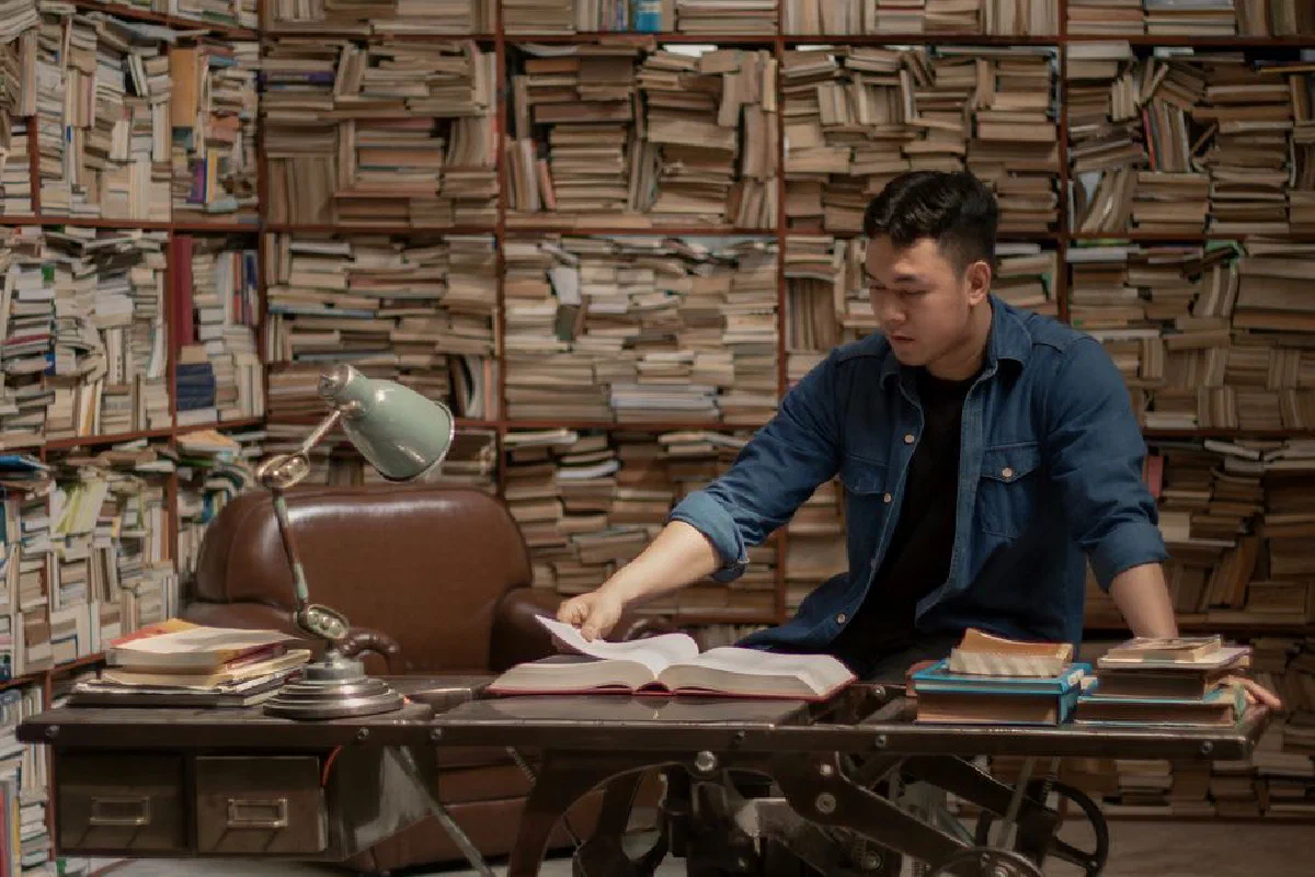 Man studying in a vintage library surrounded by books. Cozy and classic reading scene.