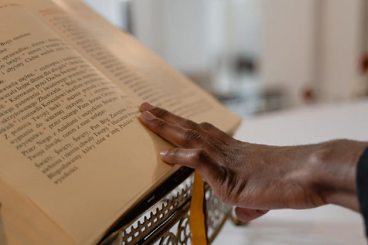 Close-up of a hand touching a religious text on a stand, symbolizing faith and spirituality.