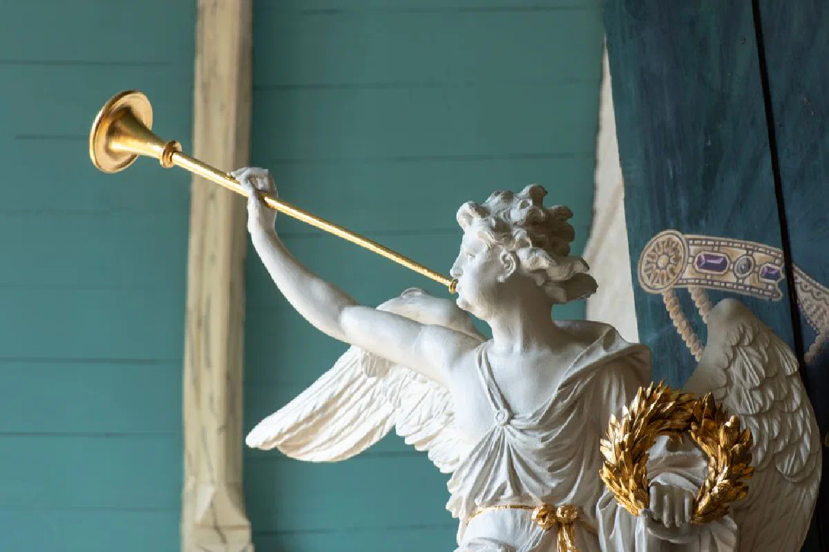 Statue of an angel blowing a golden trumpet, inside a historic church.