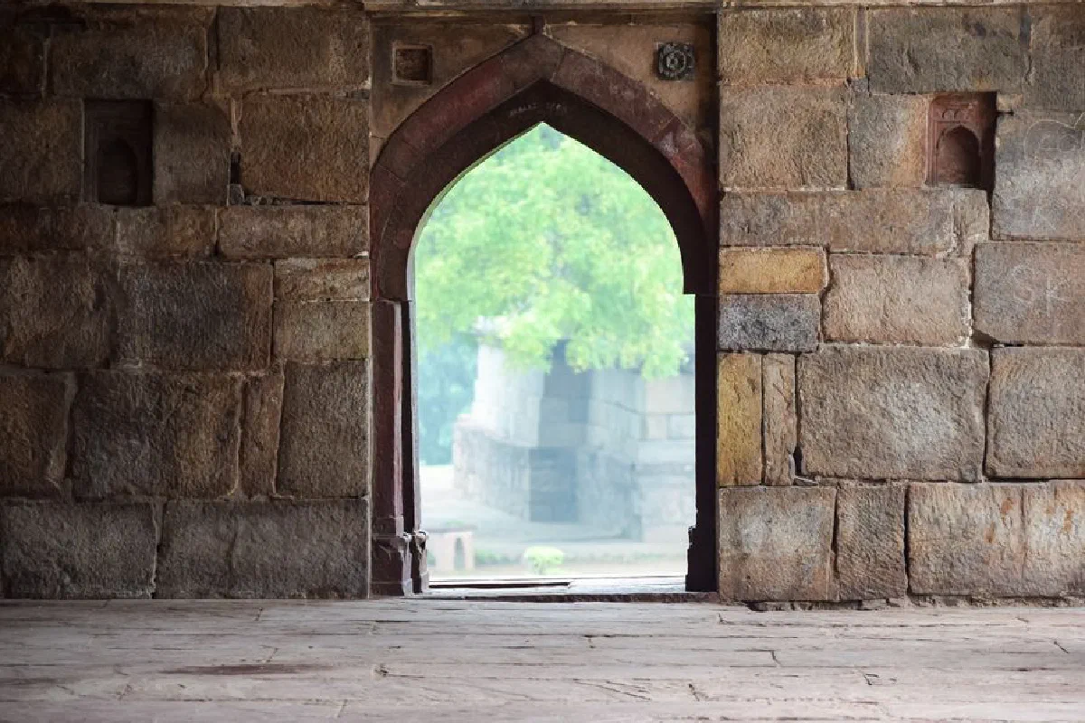 A beautiful stone archway from an ancient structure opens to a lush green garden.